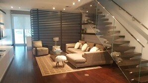 A modern living room with a glass staircase, a sofa set, and a coffee table.