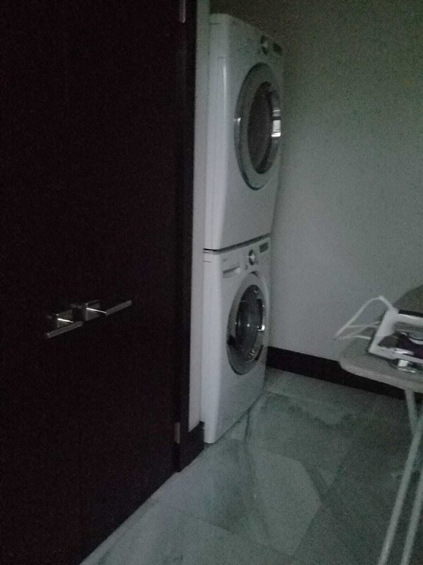 Habitación pequeña con lavadora y secadora, una mesita y una puerta.