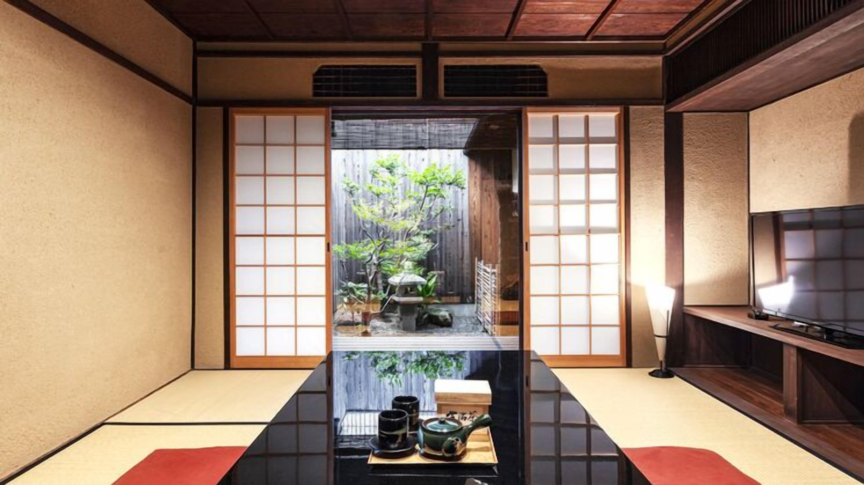 A traditional Japanese room with tatami flooring, sliding doors, a low table with tea set, and a TV on the right.