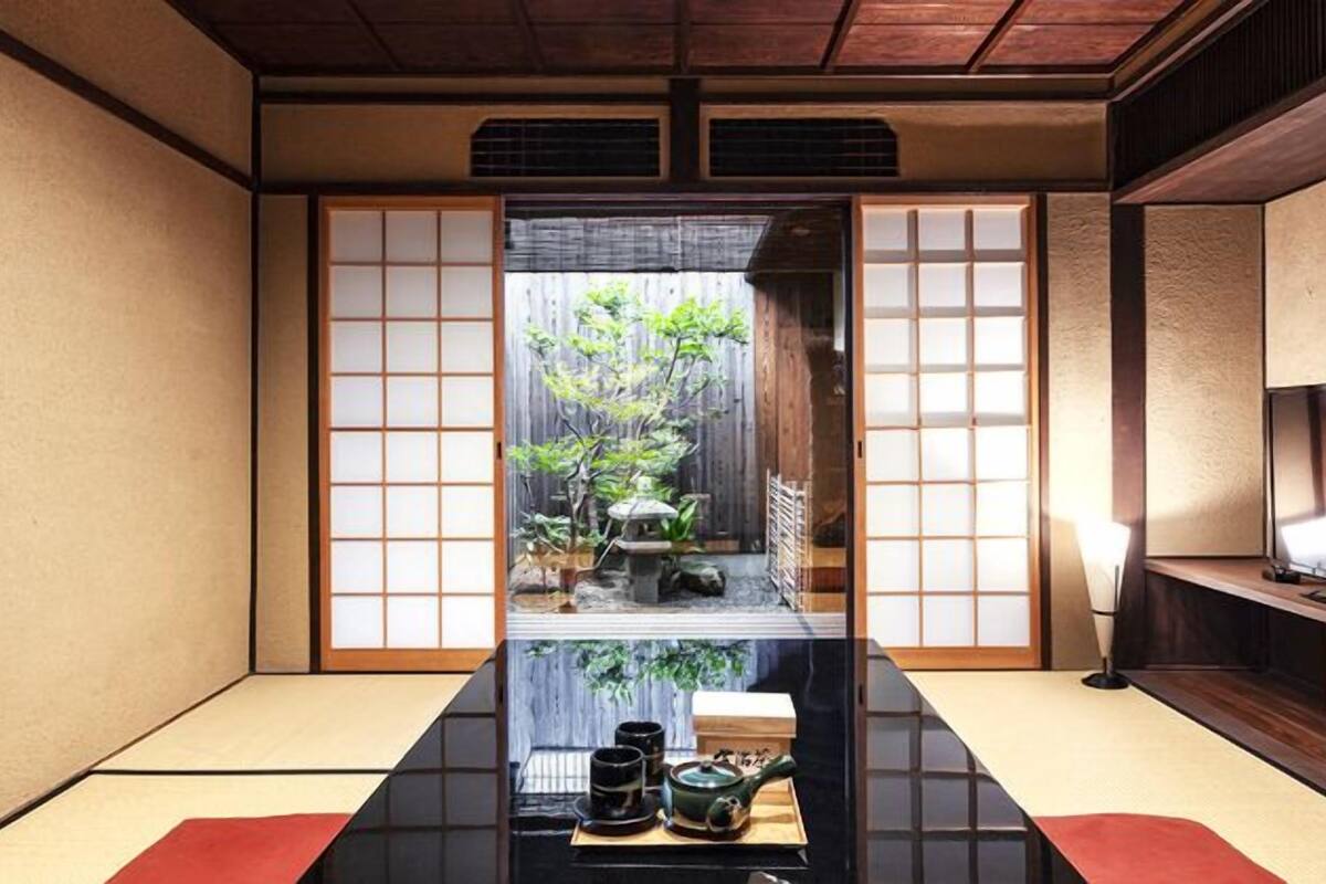 A traditional Japanese room with tatami flooring, sliding doors, a low table with tea set, and a TV on the right.
