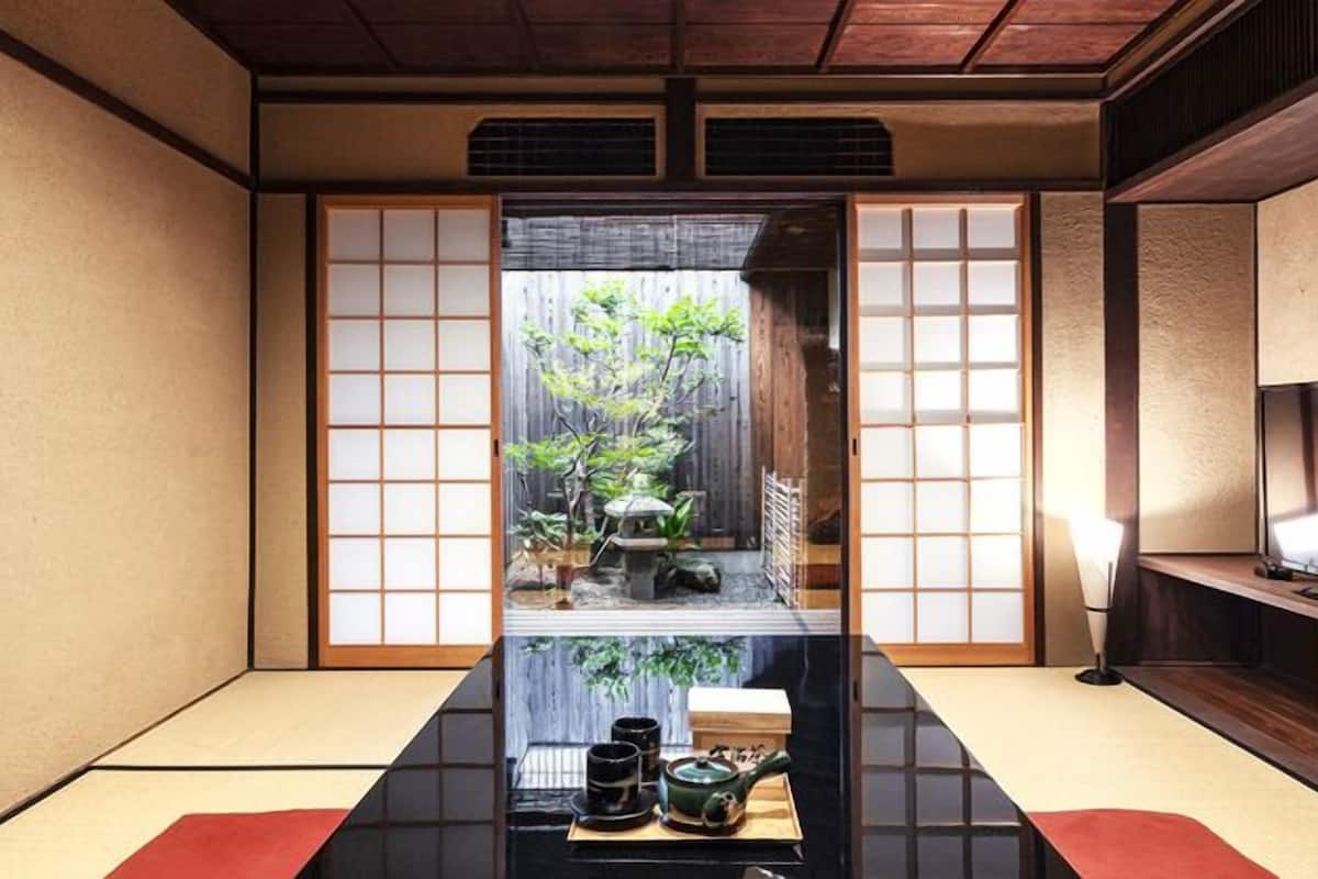 A traditional Japanese room with tatami flooring, sliding doors, a low table with tea set, and a TV on the right.