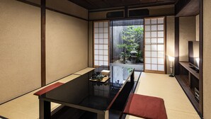 A traditional Japanese room with tatami flooring, a low table with a black top, and a sliding shoji screen door leading to a garden. - Rinn Premium Yae  (Kyoto)