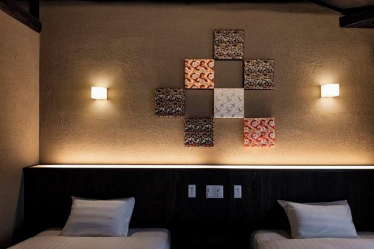 Una habitación de hotel con dos camas, una obra de arte en la pared y dos luces también fijadas a la pared.