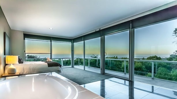 Un dormitorio moderno con una bañera grande, una cama y un balcón con vistas panorámicas.