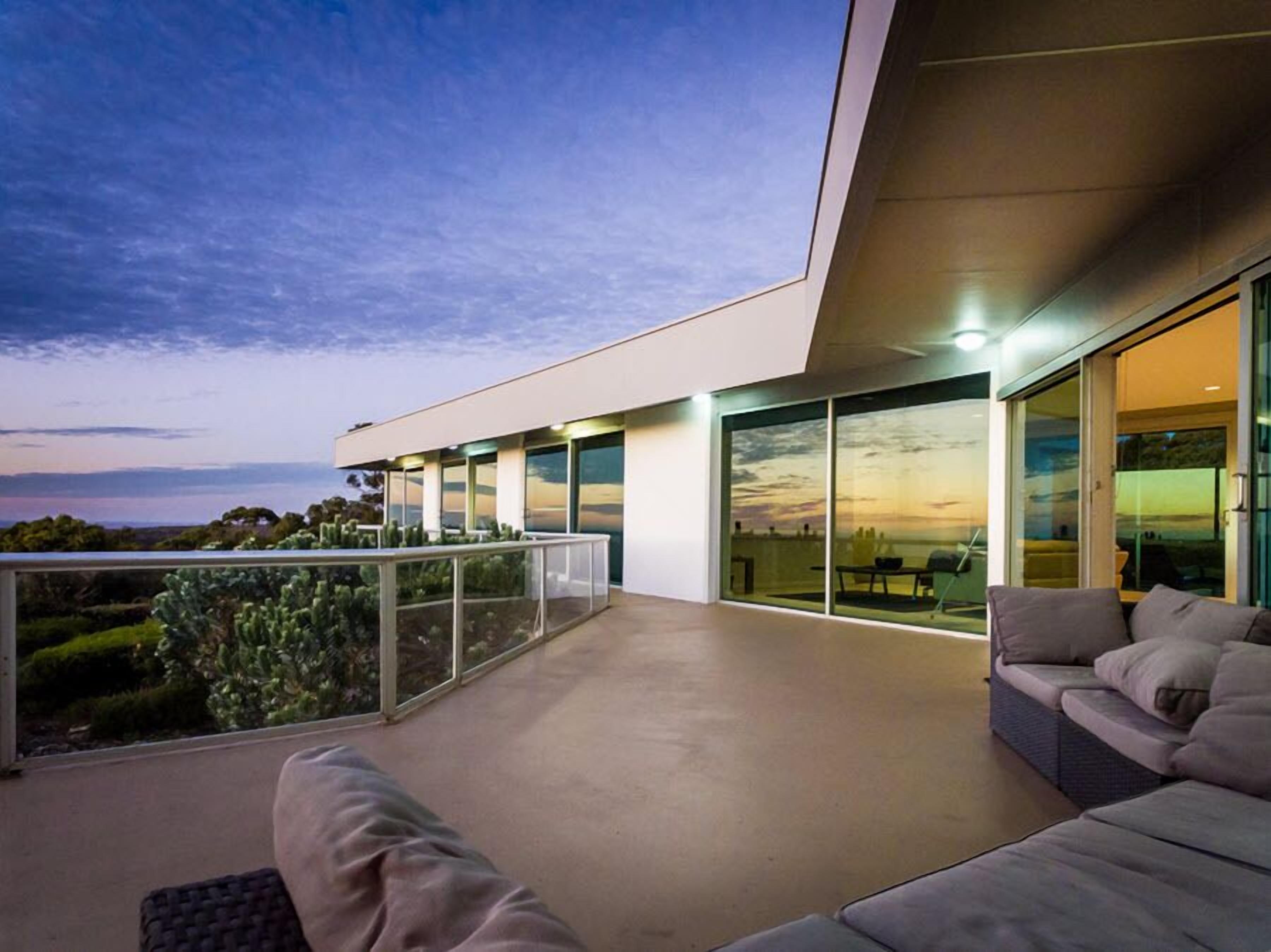 A modern outdoor living area with a glass balustrade, a sofa, and a view of the landscape.