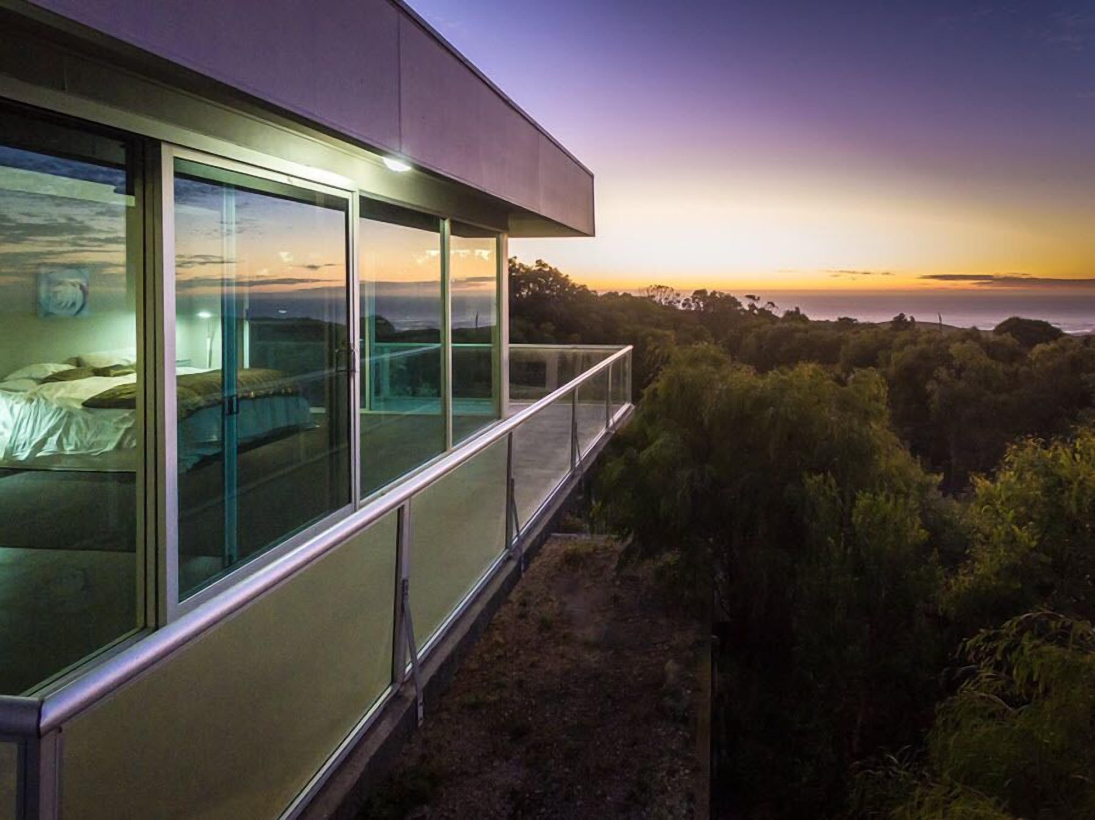 Un bâtiment moderne doté de grandes fenêtres en verre et d’un balcon donnant sur une zone boisée.
