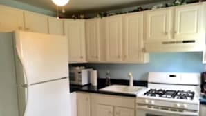 Una cocina con armarios blancos, un refrigerador, un microondas, una estufa y un lavaplatos.