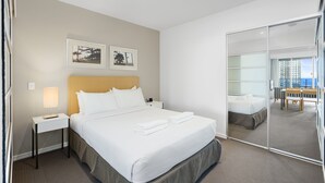 A hotel room with a large bed, a nightstand, a lamp, two framed pictures on the wall, and a sliding glass door leading to a balcony with a view of buildings. - Apartment 11504 is a holiday makers dream. Boasting a prime location (Surfers Paradise)