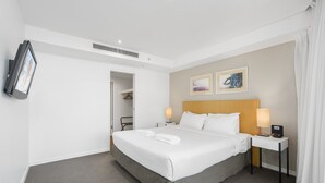 A hotel room with a large bed, two bedside lamps, a flat-screen TV mounted on the wall, and a small table with a lamp. - Apartment 11504 is a holiday makers dream. Boasting a prime location (Surfers Paradise)