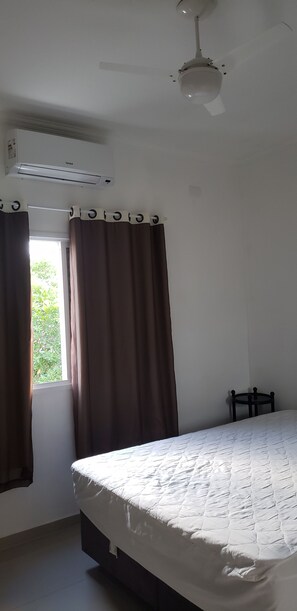 Un dormitorio con cama, ventilador de techo, equipo de aire acondicionado y ventana con cortinas.