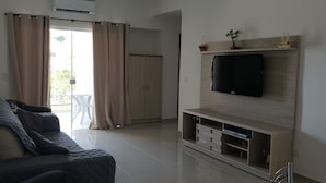 Un salón con sofá, televisor y puerta corrediza de vidrio que da a un balcón.