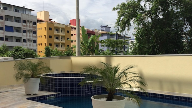 Una piscina en la azotea con suelo de baldosas, rodeada de plantas en macetas y vistas a edificios residenciales.