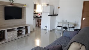 Una sala de estar moderna con televisor de pantalla plana, un sofá y una cocina al fondo.