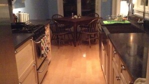 A narrow kitchen with wooden cabinets, a dining table with chairs, and a stove.