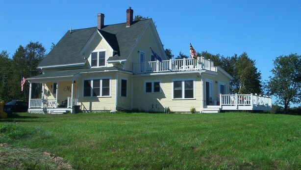 A large two-story house with a balcony, a porch, and a flag.