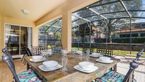 Un área de comedor al aire libre con cerramiento de vidrio, suelo de baldosas y vista del paisaje circundante.