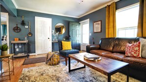 Ein Wohnzimmer mit blauer Wand, einem braunen Ledersofa, einem Couchtisch aus Holz und einem blauen Sessel.