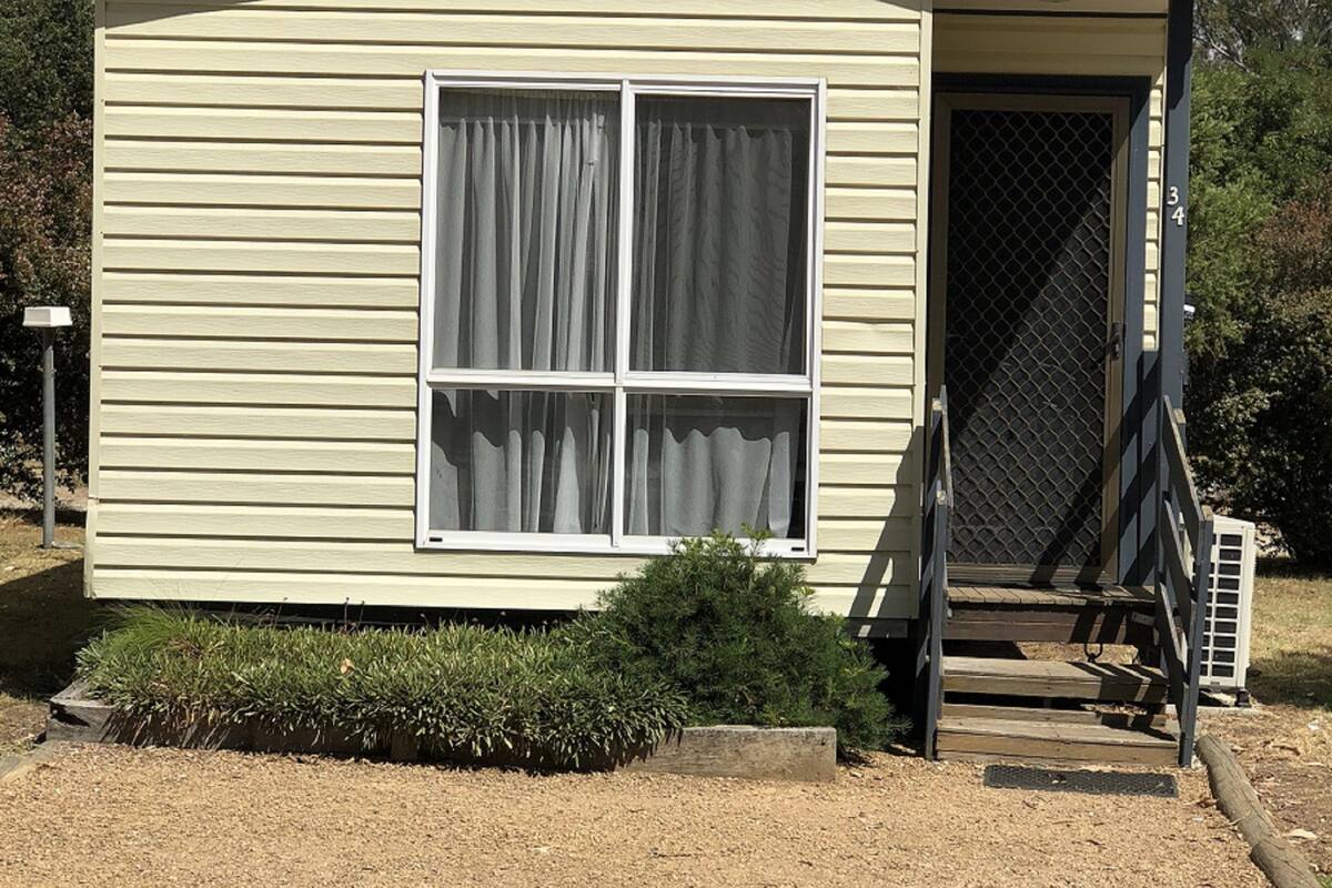 A small, single-story building with a flat roof and a sign that reads "Jayco". It has a large window with curtains, a door with a metal grid, and a small set of wooden steps leading to the entrance.