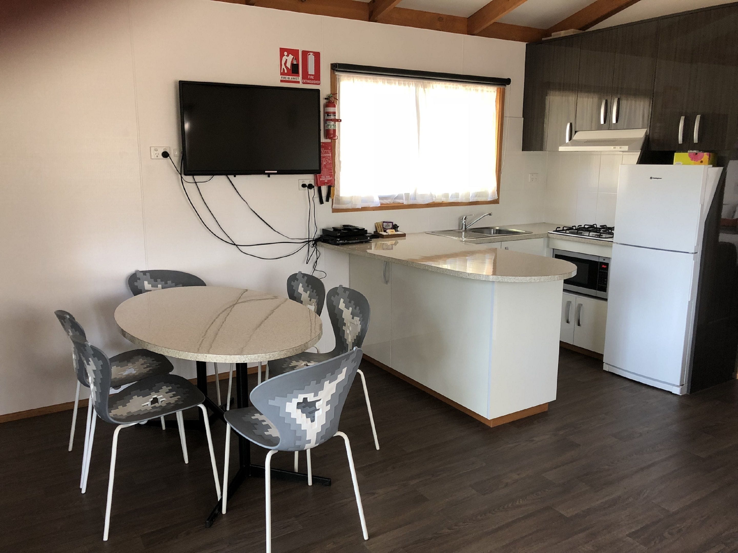 A compact kitchen with a dining area, including a round table and chairs, a built-in oven, and a refrigerator.