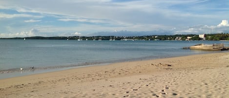 A sandy beach with footprints, a calm sea, and sailboats in the distance.
