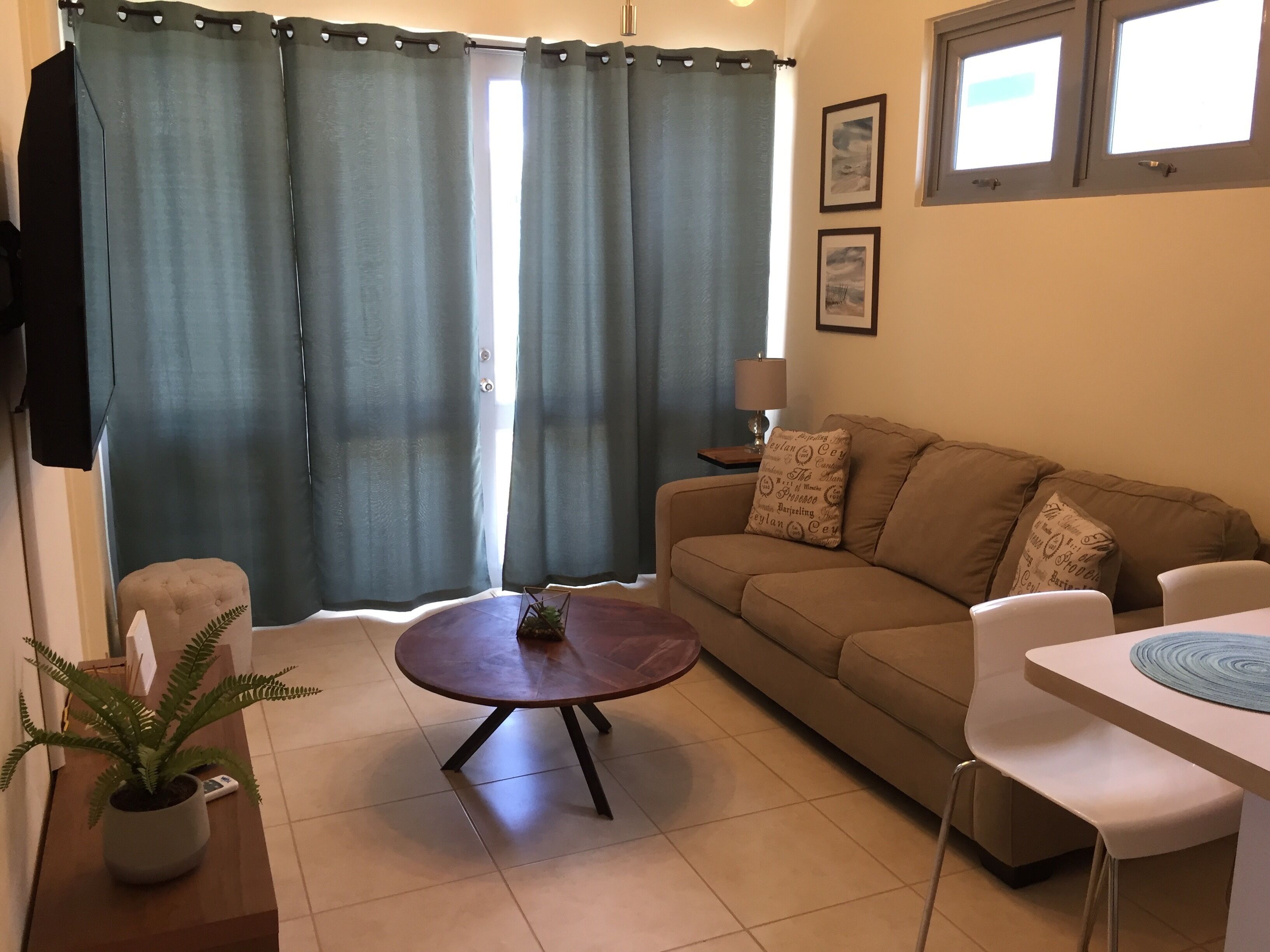 A living room with a sofa, a coffee table, a dining table, a potted plant, and a window with curtains.