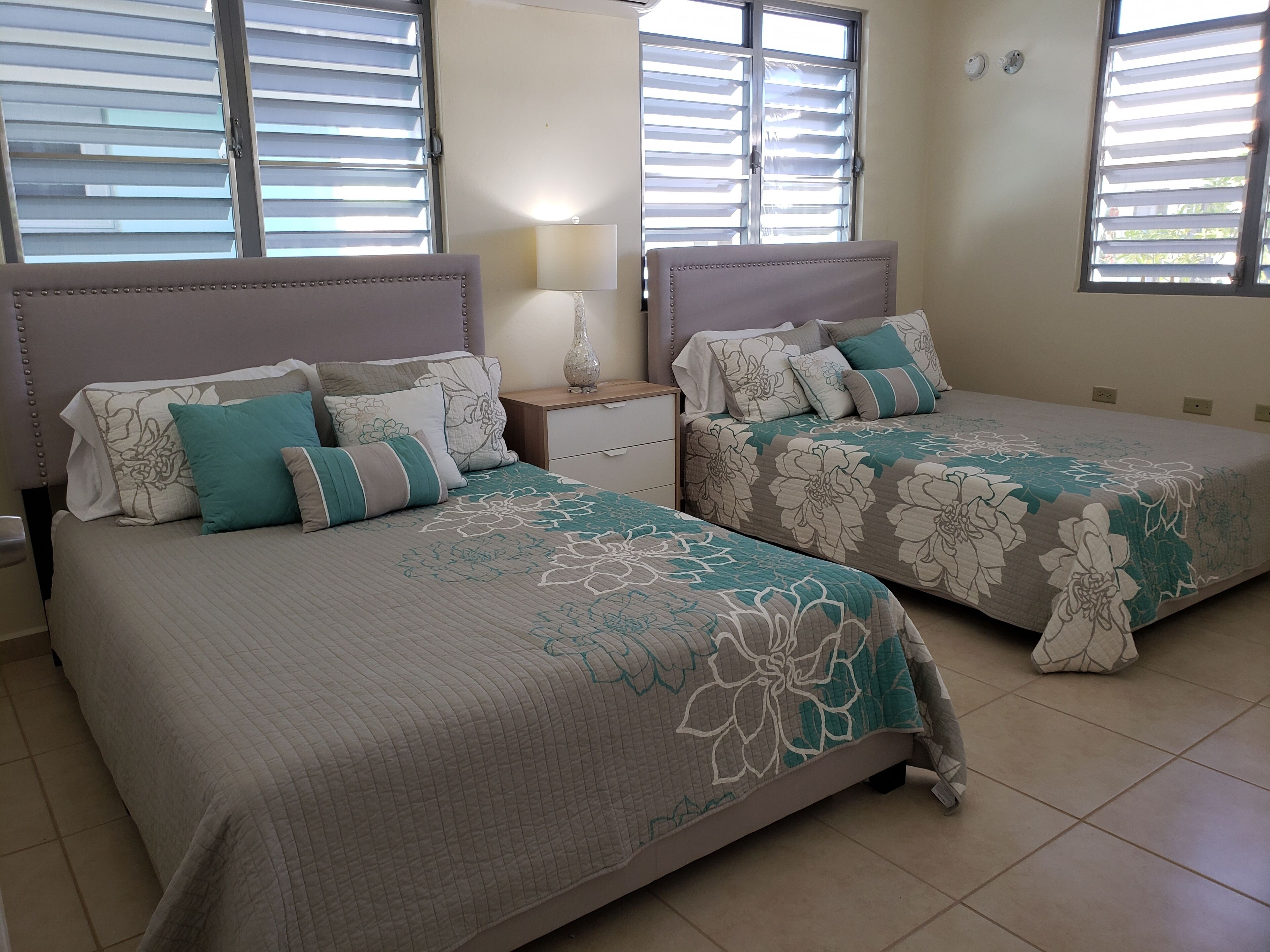 A bedroom with two beds, each with floral bedding and a headboard. There is a nightstand with a lamp between the beds.