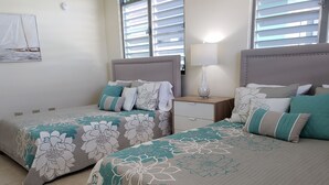 Un dormitorio con dos camas, cada una con ropa de cama floral, una mesita de noche con lámpara y una ventana con persianas.