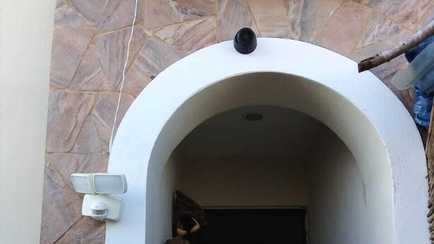 Un arco de entrada con un muro de piedra, una cámara de seguridad y una puerta con grafitis.