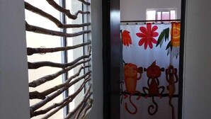 Un pasillo con una ventana cubierta por listones de madera, una puerta con un cortinero de colores con diseños de monos y una pared lisa.