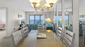 Une salle à manger spacieuse avec un plafond haut, de grandes fenêtres offrant une vue sur la mer et un lustre.