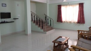 A spacious living room with a staircase, a flat-screen TV mounted on the wall, a wooden coffee table, and a striped sofa. - Spacious Beautifuly Furnished 3 Bedroom, Hall & Kitchen apartment. (Hyderabad)