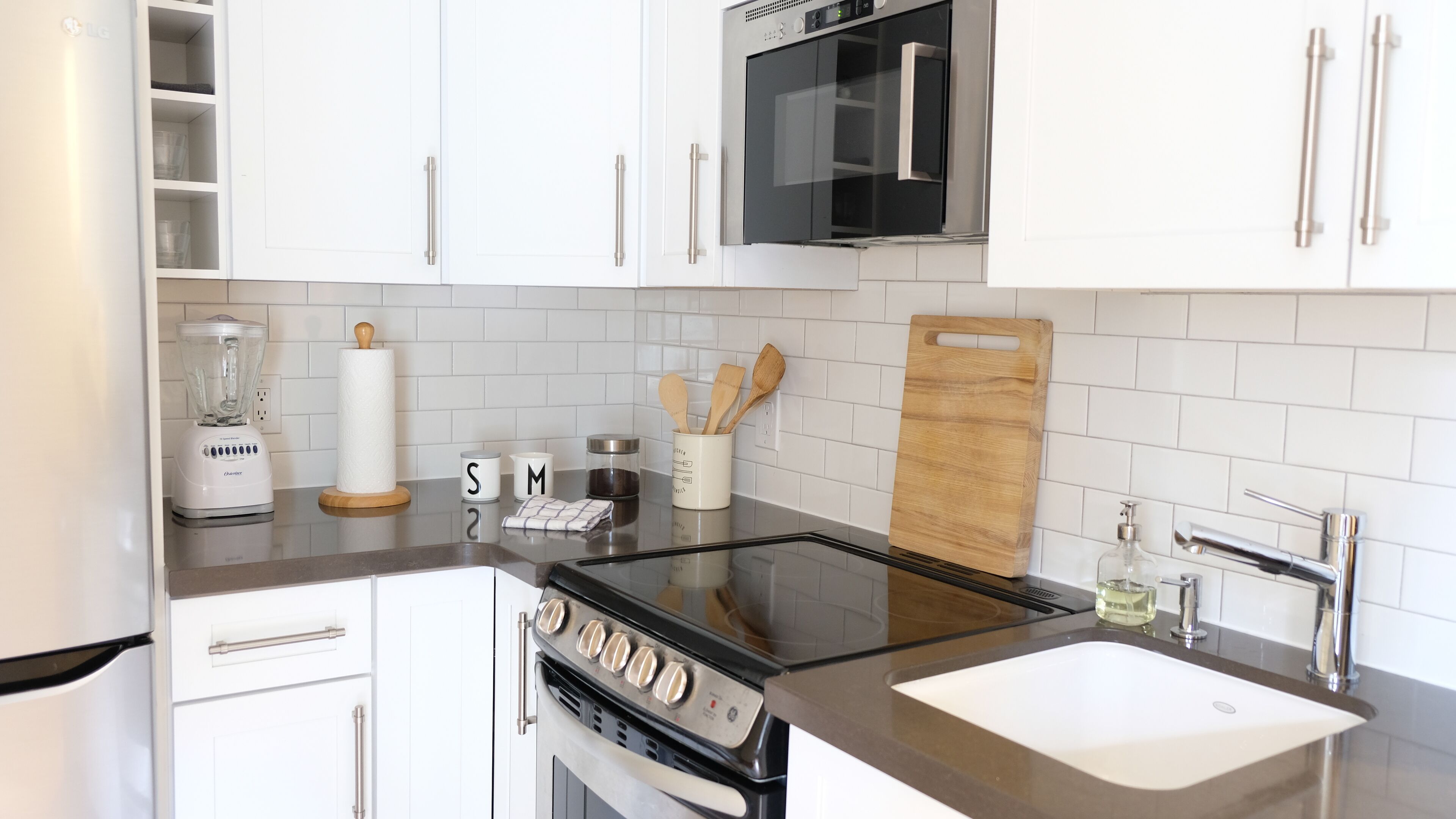 A modern kitchen with white cabinets, a black stove, a microwave, and a sink.
