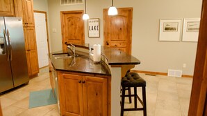 A kitchen with wooden cabinets, a stainless steel refrigerator, a granite countertop, and a bar stool. - Spacious 3 bed/2 bath Condo closest to Bridges Bay Amenities (Okoboji)