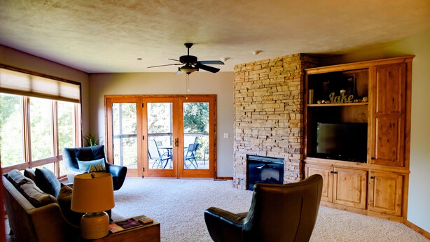 A living room with a stone fireplace, a television, and a ceiling fan. - Spacious 3 bed/2 bath Condo closest to Bridges Bay Amenities (Okoboji)