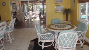 A room with yellow walls, white wicker furniture, a tiled floor, and a view through a glass door to an outdoor patio area.