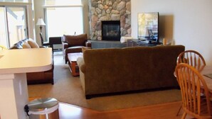 A living room with a stone fireplace, a television, and a dining area with wooden furniture. - Family Retreat at Cedar River (Bellaire)