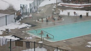 A pool area with a hot tub and a smaller pool, surrounded by snow-covered ground and a metal fence. - Family Retreat at Cedar River (Bellaire)