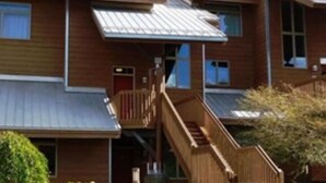 A multi-story wooden building with a metal roof, a staircase leading to the entrance, and a small porch area. - Family Retreat at Cedar River (Bellaire)