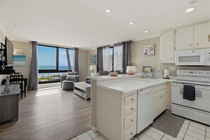 A modern kitchen with a large island, a dining area with a view, and a living space with a sofa and a table.
