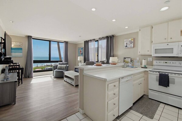 A modern kitchen with a large island, a dining area with a view, and a living space with a sofa and a table.