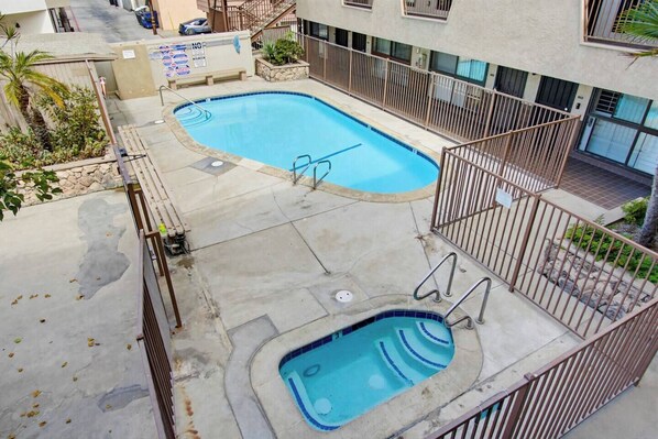 Une piscine sur le toit, dotée d’un jacuzzi, entourée d’une clôture en métal, avec un bâtiment visible en arrière-plan.