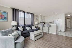 A modern living room with a sofa, a coffee table, and a dining area with bar stools.