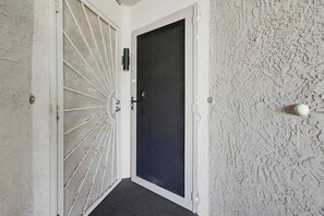 Un pasillo con pared texturizada, una puerta con panel negro y una puerta blanca con diseño de malla.