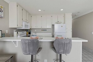 A modern kitchen with white cabinets, a white countertop, and two grey bar stools.