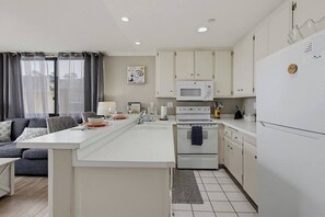 Une cuisine moderne avec des meubles blancs, un îlot central, un four à micro-ondes, un four et un réfrigérateur.