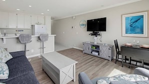 Ett modernt vardagsrum med en soffa, ett matbord och en köksdel med skåp och en tv.