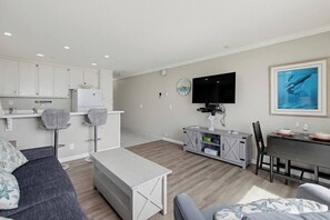 Un salon moderne comprenant un canapé, une table à manger et un coin cuisine avec des placards et un téléviseur.