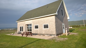 A single-story house with a sloped roof, a front porch, and a picnic table. - New  Beachfront  Post+beam Cottage, Amazing Sunsets and Just Off Cabot Trail (Point Cross)