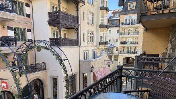 A balcony with a glass table and wicker chairs, overlooking a street with shops and a building with a clock. - 1 min. walk to Ski Lift/Gondola, shopping & dining! Perfect location!New Remodel (Vail)