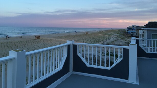 A beach view from a balcony with a white railing, sandy beach, and ocean in the background. - LBI Oceanfront. Beautiful! Views galore. Dine overlooking the dunes. (Beach Haven Crest)